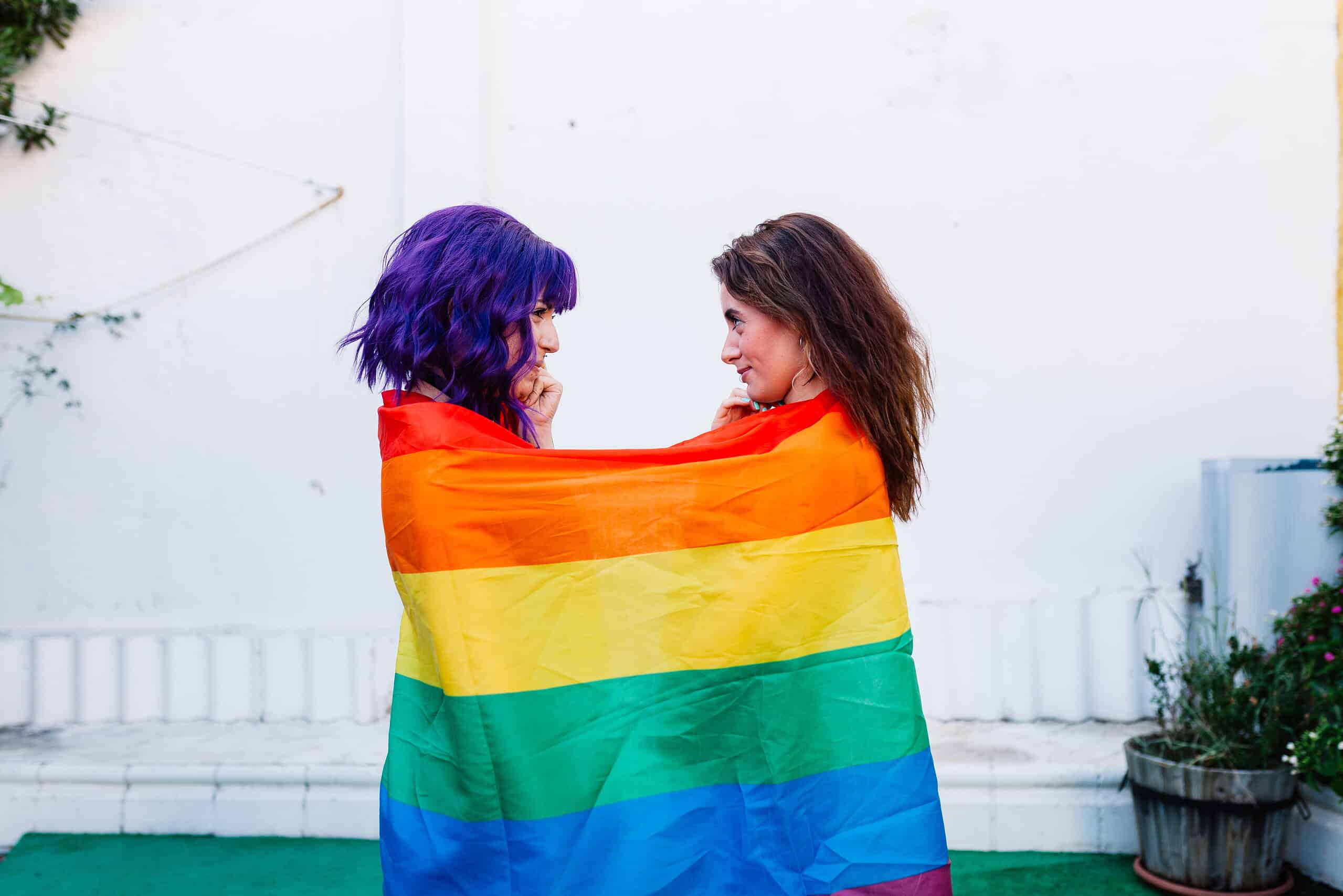 Duas mulheres frente a frente envolvidas por bandeira arco-iris